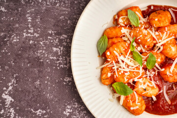 Plate of tasty gnocchi with tomato sauce and cheese on grey background