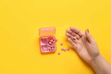 Female hand and container with pills on yellow background