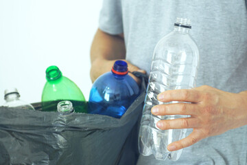 Everyday eco habit: sorting packaging for recycling. Focus on conscious living: a man holds a used transparent plastic bottle in one hand and a full garbage bag in the other. Waste separation