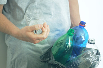 Sorting plastic waste at home: а man puts empty bottles without caps in a black garbage bag, symbolizing environmental care and household recycling habits. Eco responsibility and sustainable lifestyle