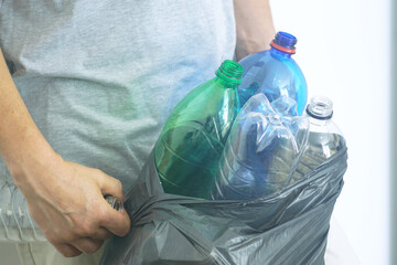 Collection and separation of household waste: сlose-up of man’s hands holding full trash bag with used plastic bottles. Eco-awareness, environmental responsibility and conscious waste management