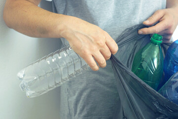 Waste separation: a man collects empty bottles in a garbage bag for subsequent recycling, close-up...