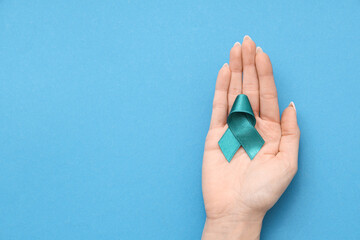 Female hand with teal ribbon on blue background. Sexual Assault Awareness Month