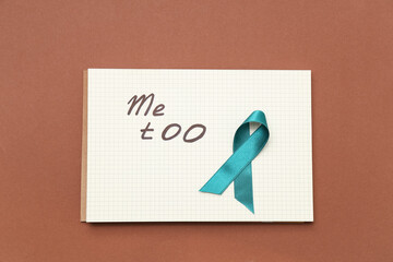 Teal ribbon and notebook with text ME TOO on brown background. Sexual Assault Awareness Month