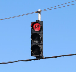 Red traffic light for bicycles hanging from wires with the sky as background.