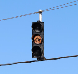 Yellow traffic light for bicycles hanging from wires with the sky as background.