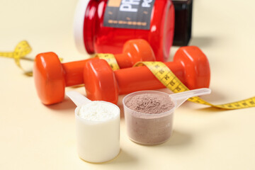 Scoops with protein powder, dumbbells and measuring tape on color background