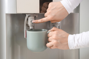 Female hands filling cup with filtered water from cooler in room