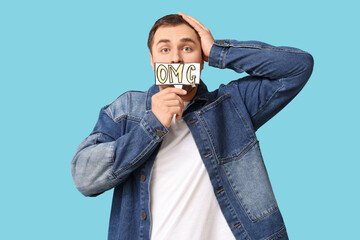 Shocked young man holding text OMG on blue background