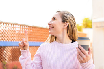 Young blonde woman holding a take away coffee at outdoors intending to realizes the solution while...