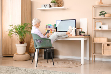 Young female designer sitting at table with computer and holding mobile phone in light office