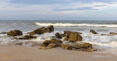 A beach of coquina rocks is sculpted by the sea in this evening landscape view with soft water at River to Sea Preserve