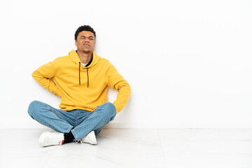 Young African American man sitting on the floor isolated on white background suffering from...