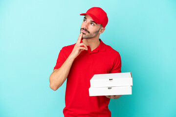 Delivery caucasian man picking up pizza boxes isolated on blue background looking up while smiling