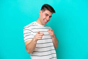 Young caucasian man isolated on blue background surprised and pointing front