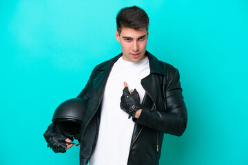 Young caucasian man with a motorcycle helmet isolated on blue background with surprise facial...