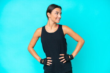 Young caucasian woman isolated on blue background posing with arms at hip and looking side