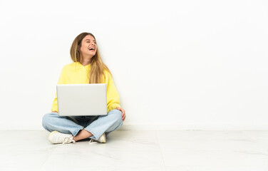 Young woman with a laptop sitting on the floor laughing in lateral position