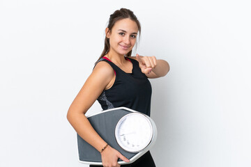 Young Ukrainian woman isolated on white background holding a weighing machine and pointing to the...