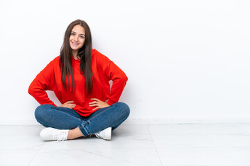 Young Ukrainian woman sitting on the floor isolated on white background posing with arms at hip and...