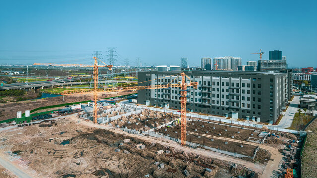 Construction site with large yellow cranes working on the foundation of a new factory building.