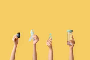 Female hands with wristwatch, male sign, light blue ribbon and water bottle on yellow background....
