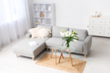 Interior of stylish living room with grey sofa, pillows and vase of lily flowers on coffee table, blurred view