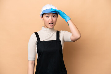 Young Chinese Fishmonger woman wearing an apron and holding a raw fish isolated on pink background doing surprise gesture while looking to the side