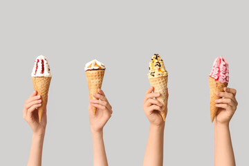 Female hands with different sweet ice-cream in waffle cones on grey background