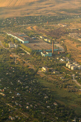 An expansive aerial view of an industrial complex and surrounding rural landscape, featuring large factory buildings, a tall chimney, and scattered residential areas
