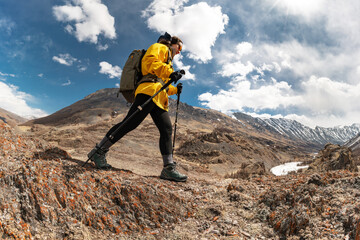 Low angle view of a girl hiker with backpack and trekking poles walking along rocky slope in Altai...
