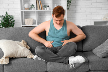 Young overweight man touching fat on his belly at home. Weight gain concept
