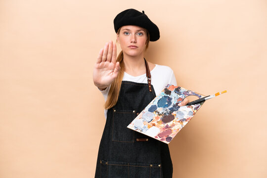 Young artist caucasian woman holding a palette isolated on beige background making stop gesture - Powered by Adobe