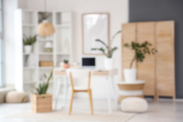 Blurred view of light office with workplace, shelf unit and folding screen