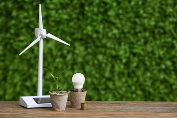 Wind turbine model with light bulb and plant on table outdoors. Green Energy concept