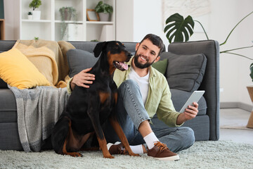 Young man with Dobermann dog using tablet computer at home