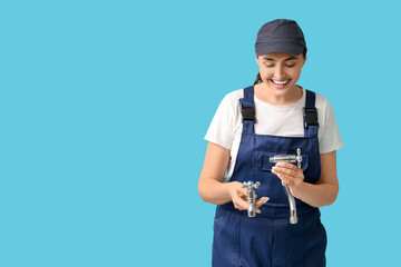 Young female plumber with faucets on blue background. Woman in male profession concept