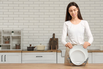 Young woman putting clean plates into rack on wooden table