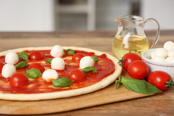 Raw pizza with mozzarella and ingredients on table in kitchen