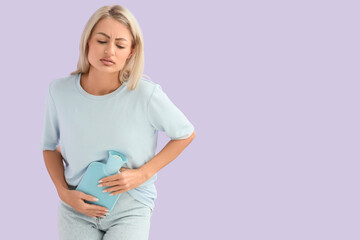 Young woman with hot water bottle suffering from menstrual cramps on lilac background