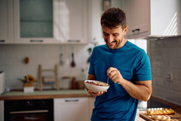 Happy man eating oatmeal with fresh fruit for breakfast.
