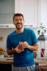 Happy man having glass of fresh smoothie in morning and looking at camera.