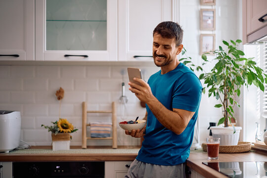 Happy man using cell phone while enjoying in healthy meal in morning.