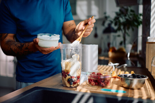 Close up of man adding Greek yogurt while preparing healthy smoothie in kitchen. - Powered by Adobe