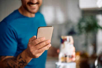 Close up of man using smart phone while making breakfast in kitchen.