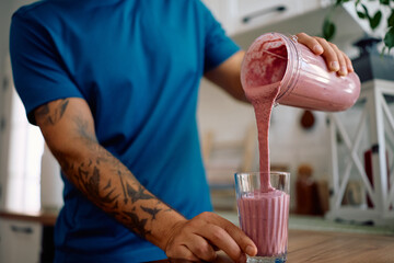 Close up of man pouring fruit smoothie in glass in kitchen.