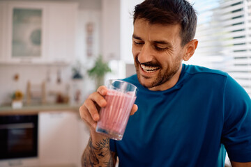 Happy man enjoying in morning while drinking smoothie at home.