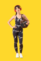 Obraz premium Young woman in headphones with sports bag on yellow background