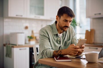 Male entrepreneur texting on cell phone while working at home.