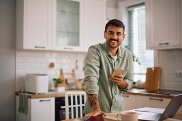 Happy entrepreneur using mobile phone while working at home and looking at camera.